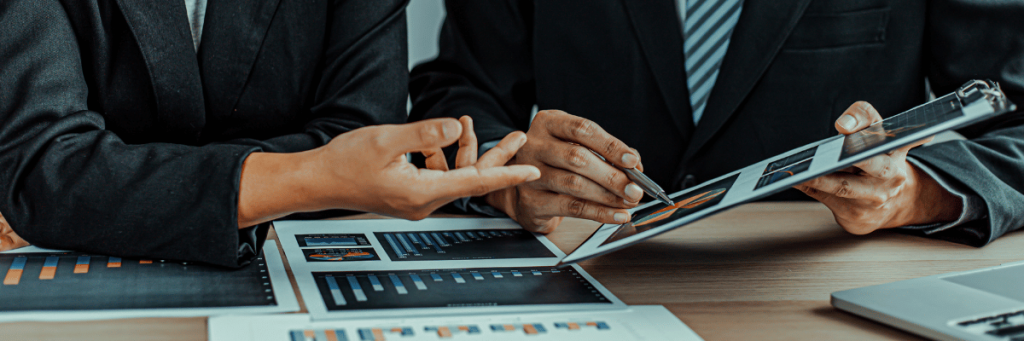 duas mãos analisando uma prancheta com gráficos.